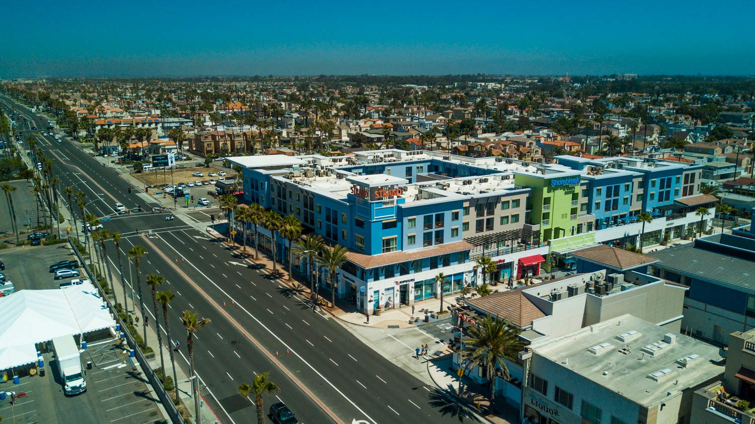 Aerial view of a colorful apartment complex beside a wide road in a suburban neighborhood
