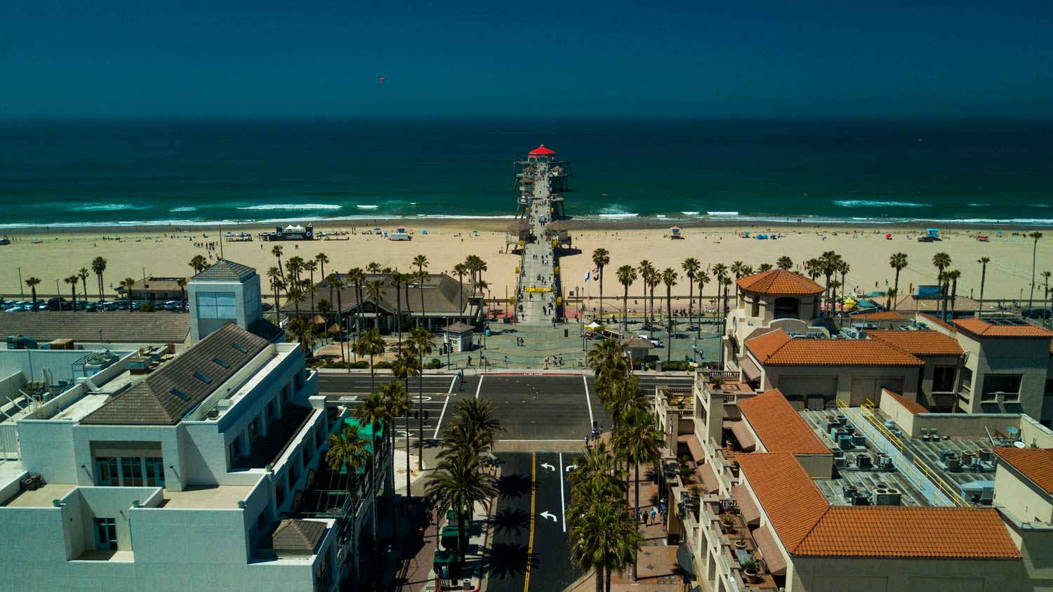 View from a rooftop over a beach town, with palm-lined streets, sand, ocean, and a lifeguard tower at sunset
