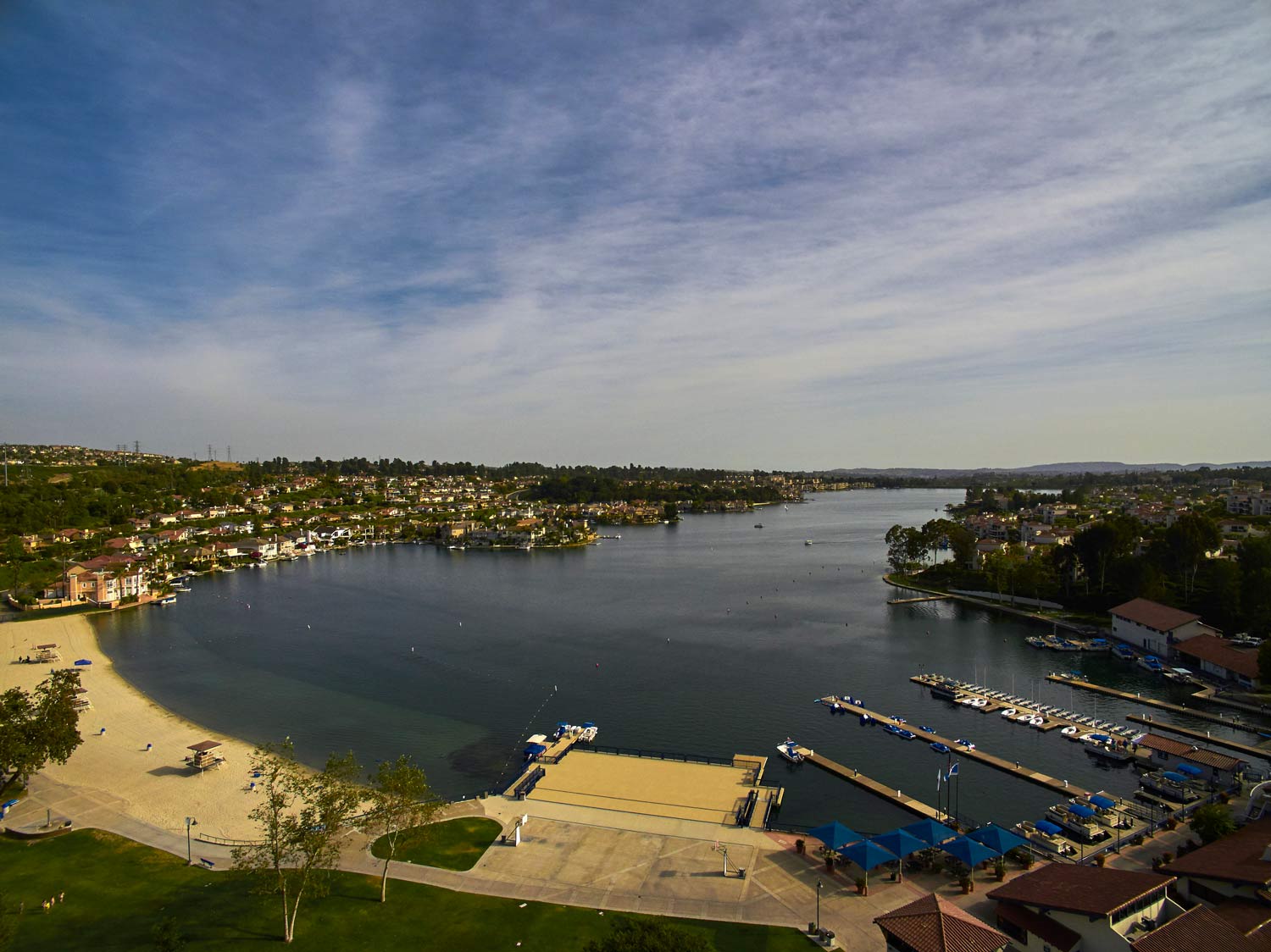 Wide river with boats and waterfront docks beside a sandy beach under a cloudy sky