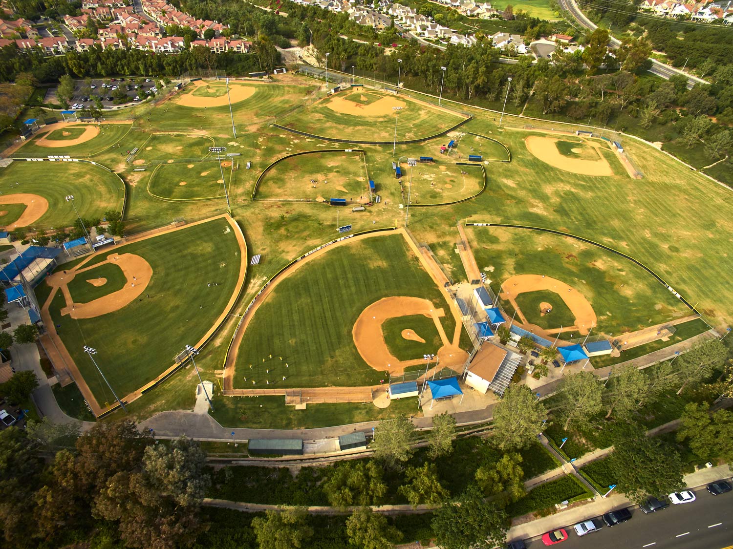 Aerial view of a baseball/softball complex with multiple green fields and brown infields surrounded by trees