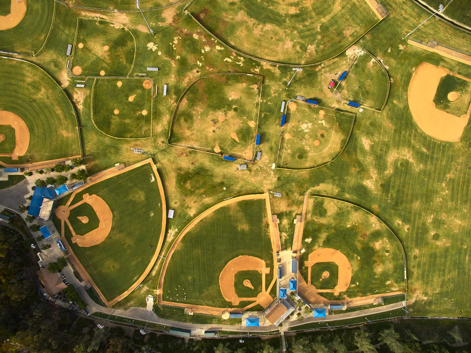 Aerial view of several baseball fields with green grass and tan infields in a park-like complex.