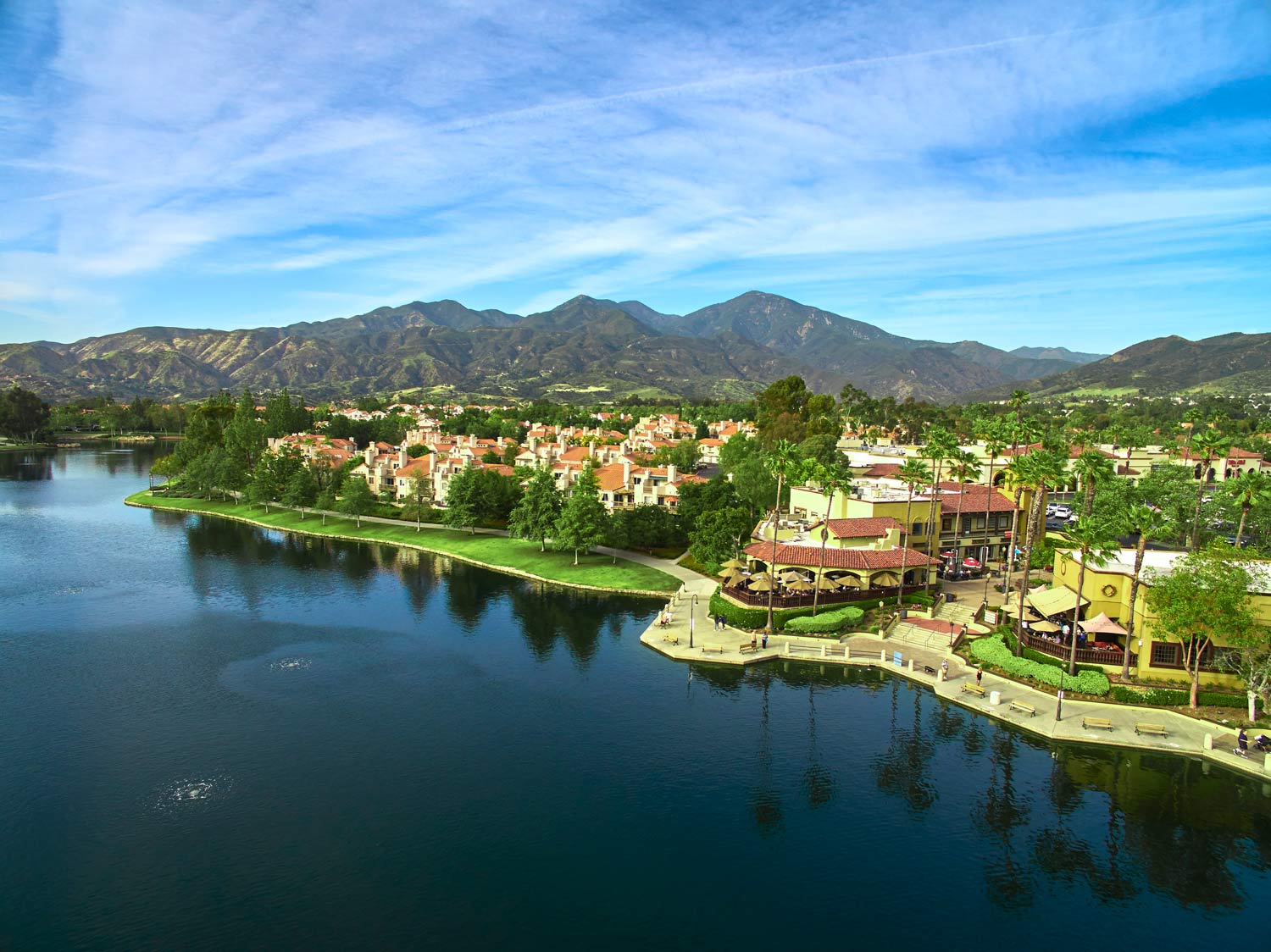Lakeside resort neighborhood with villas, palm trees, and mountains under a blue sky
