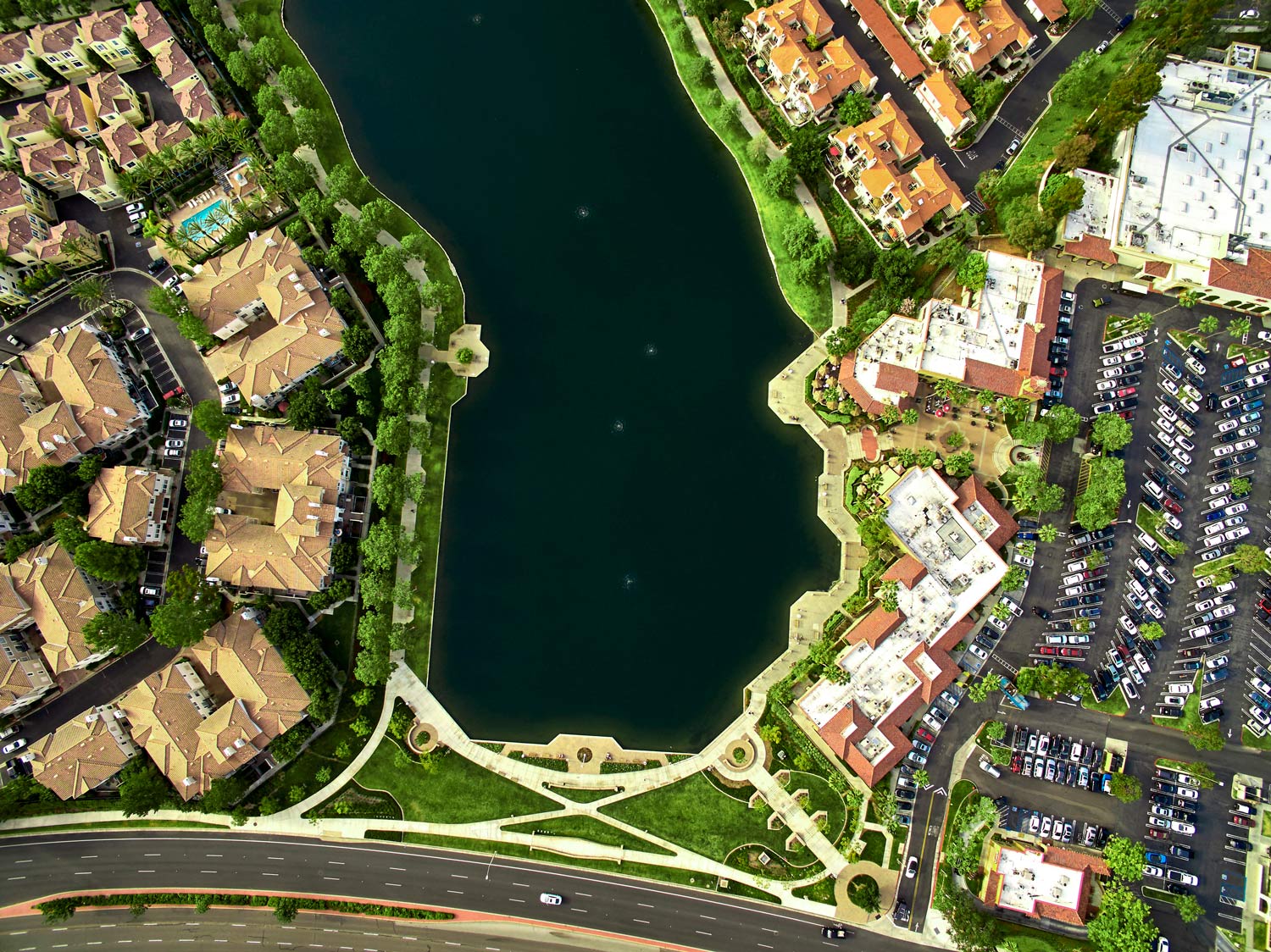 Aerial view of a lake bordered by apartment buildings, roads, and a landscaped park with walkways.
