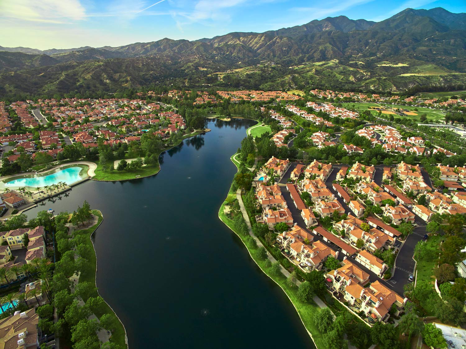 Aerial view of a lake beside red-roofed houses and mountains under clear skies
