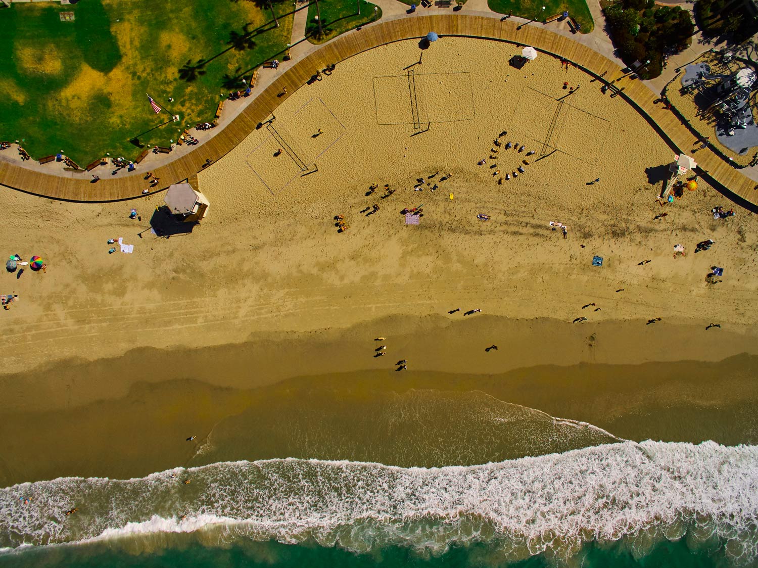 Aerial view of a crowded sandy beach with green water and waves along the shore