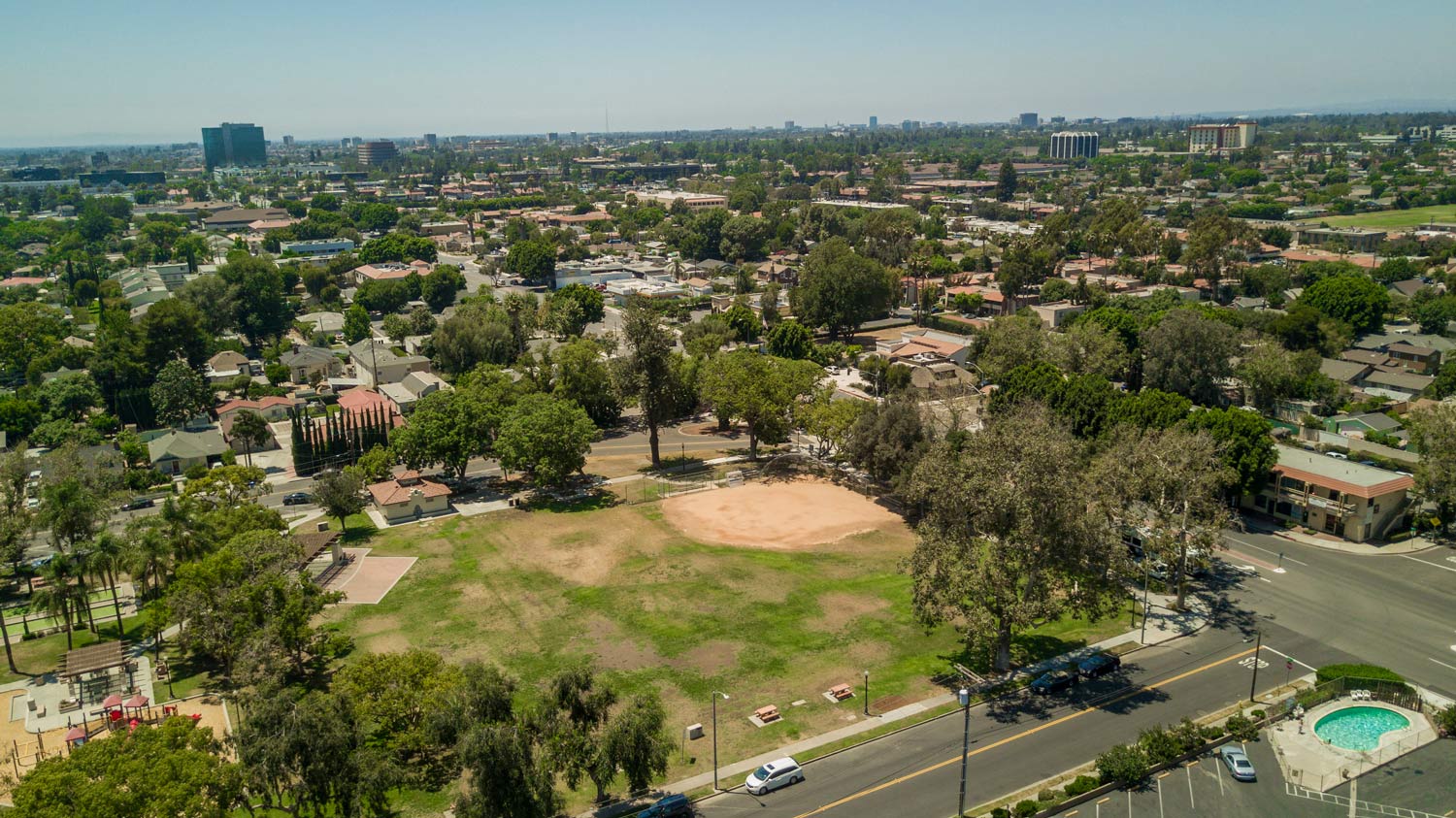Aerial view of a suburban neighborhood with a grassy park, baseball field, trees, and roads under a clear sky