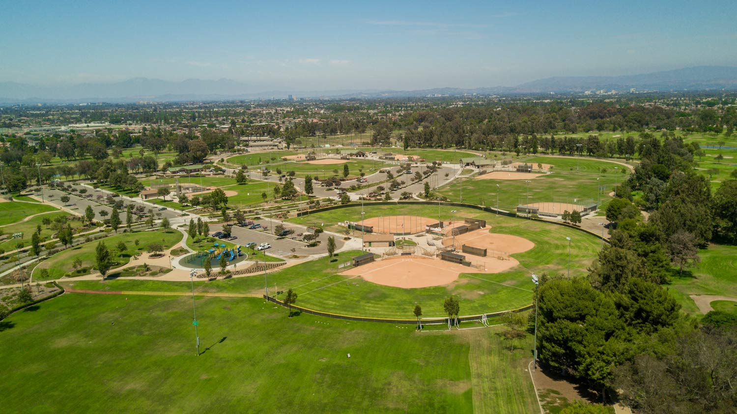 Aerial view of a green park with sports fields, trees, and city buildings in the distance