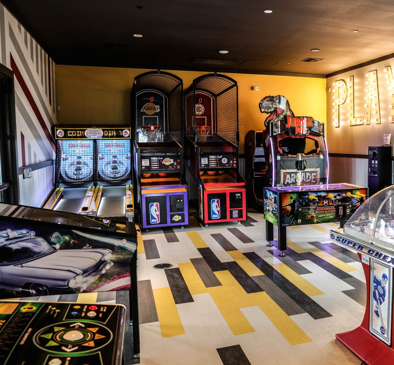 Modern arcade room with racing, arcade, and pinball machines on a patterned floor