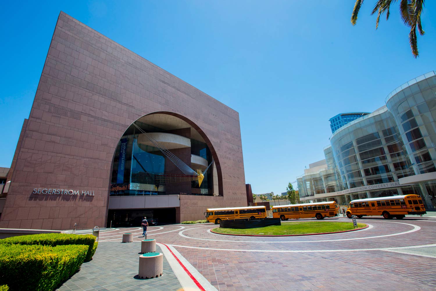 Modern brick and glass building with an arched entrance and yellow buses in a sunny courtyard