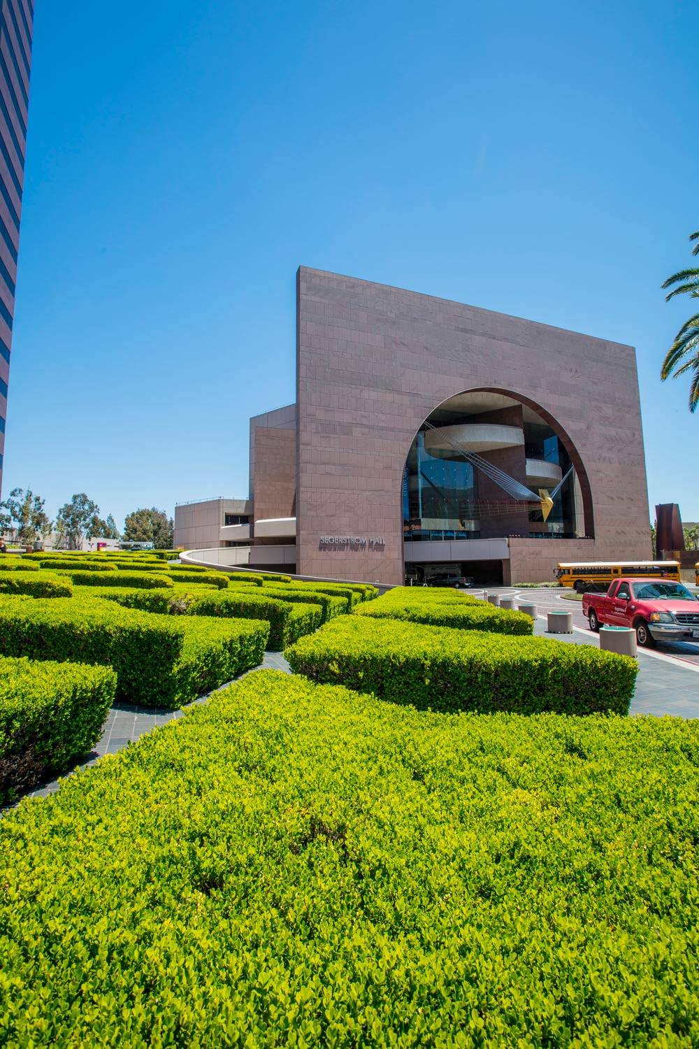 Modern brick building with arched entrance, framed by bright green hedges under a clear blue sky