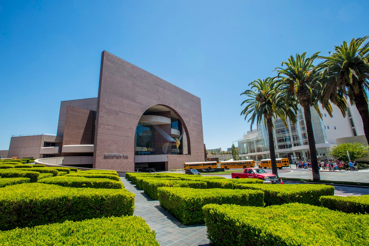 Modern brick building with an arched entrance, palm trees, and manicured green hedges under a blue sky