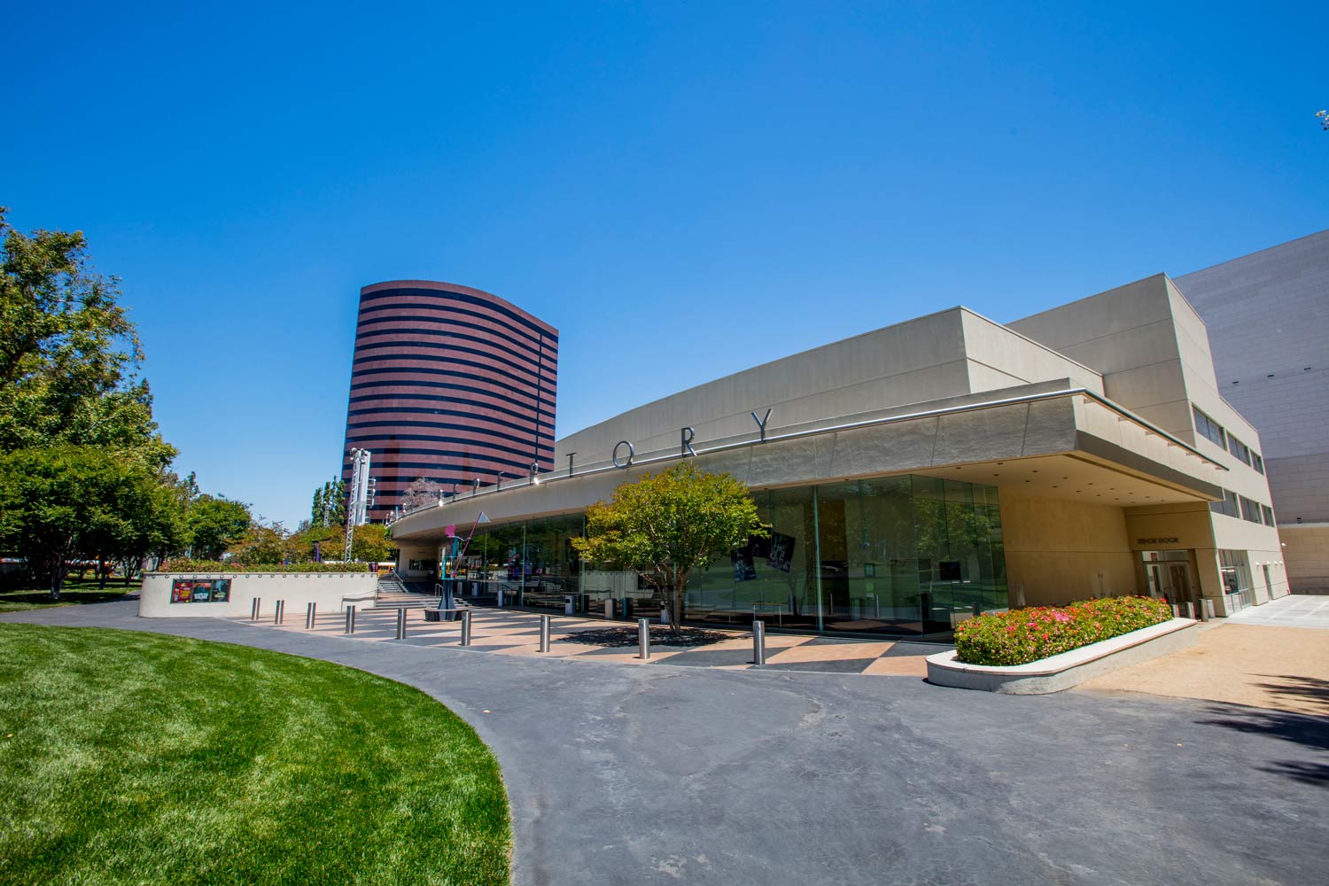 Modern building with a curved red tower, landscaped lawn, and blue sky on a sunny day