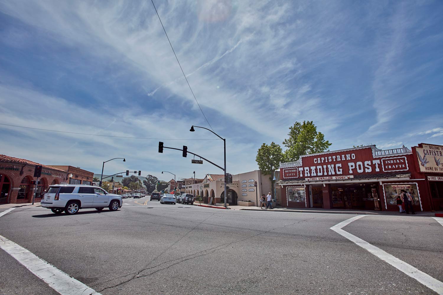 Wide street intersection with traffic lights, a white pickup truck, and a rustic red building with a sign.
