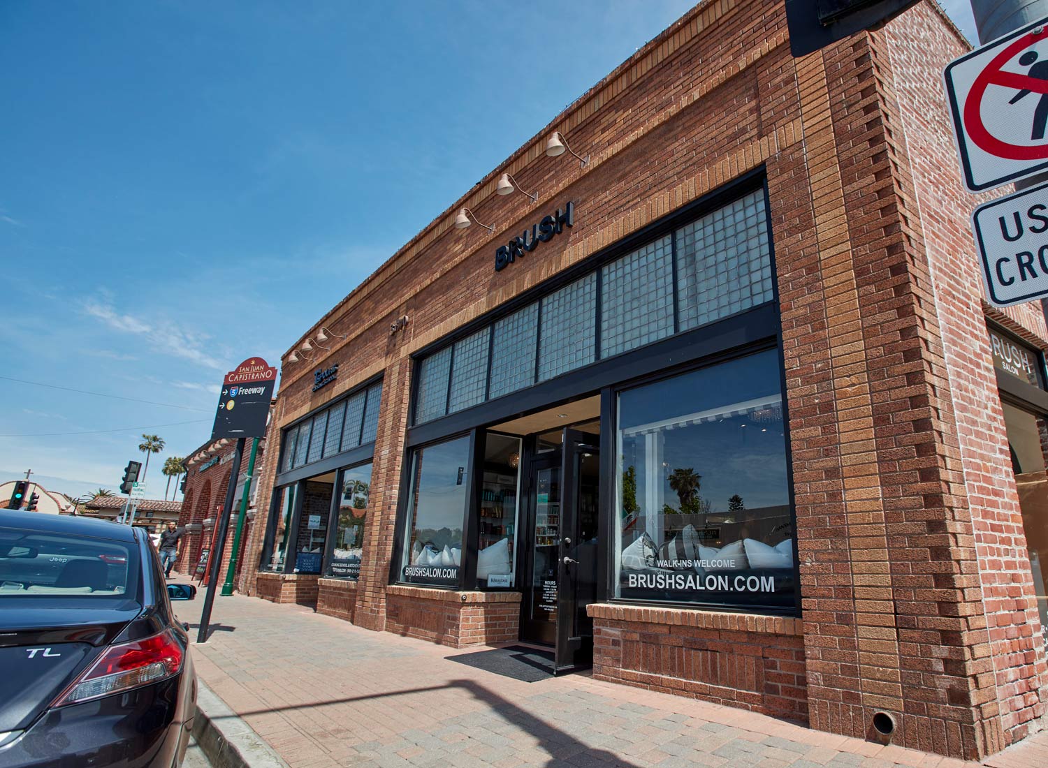 Brick storefront on a sunny street with large windows and parked cars