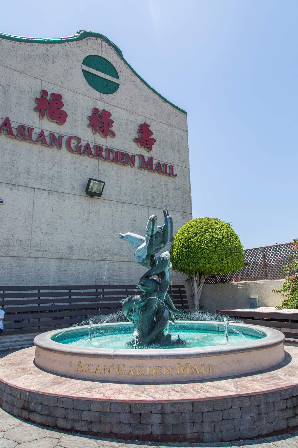 A fountain with a mermaid statue in front of the ASAHI GARDEN MALL sign under a blue sky