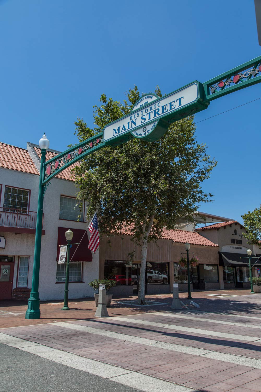 Main Street archway over a sunny pedestrian plaza with shops and a tree