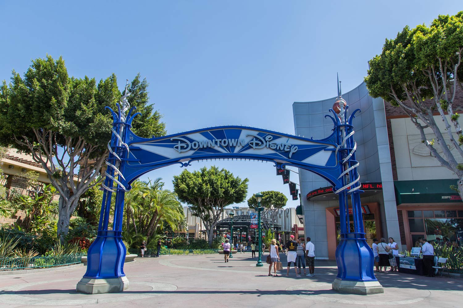 Blue archway entrance to a sunny plaza with trees and people walking nearby