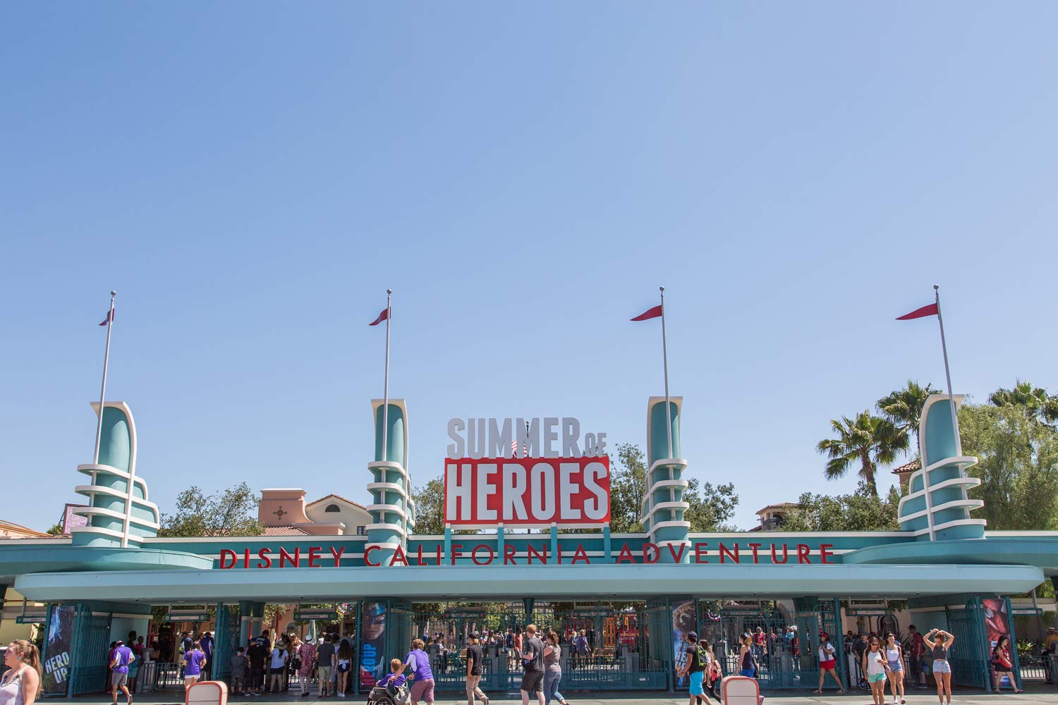 Disney California Adventure entrance with the “Summer of Heroes” sign and crowd below under a clear blue sky