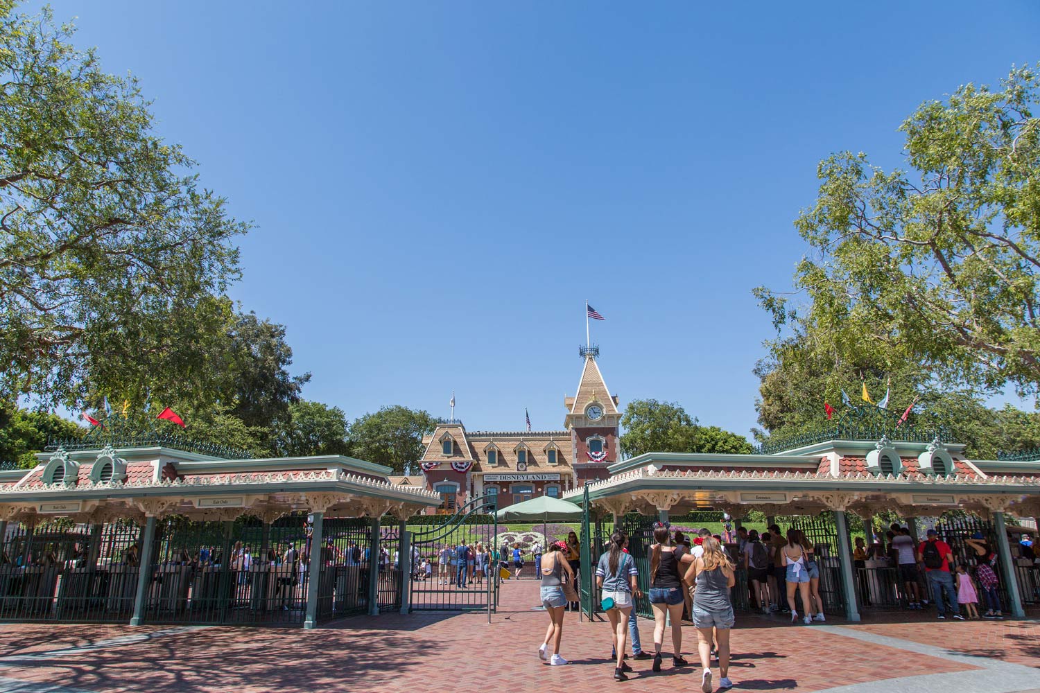 Entrance to a theme park with crowds, trees, and a clock tower under a clear blue sky