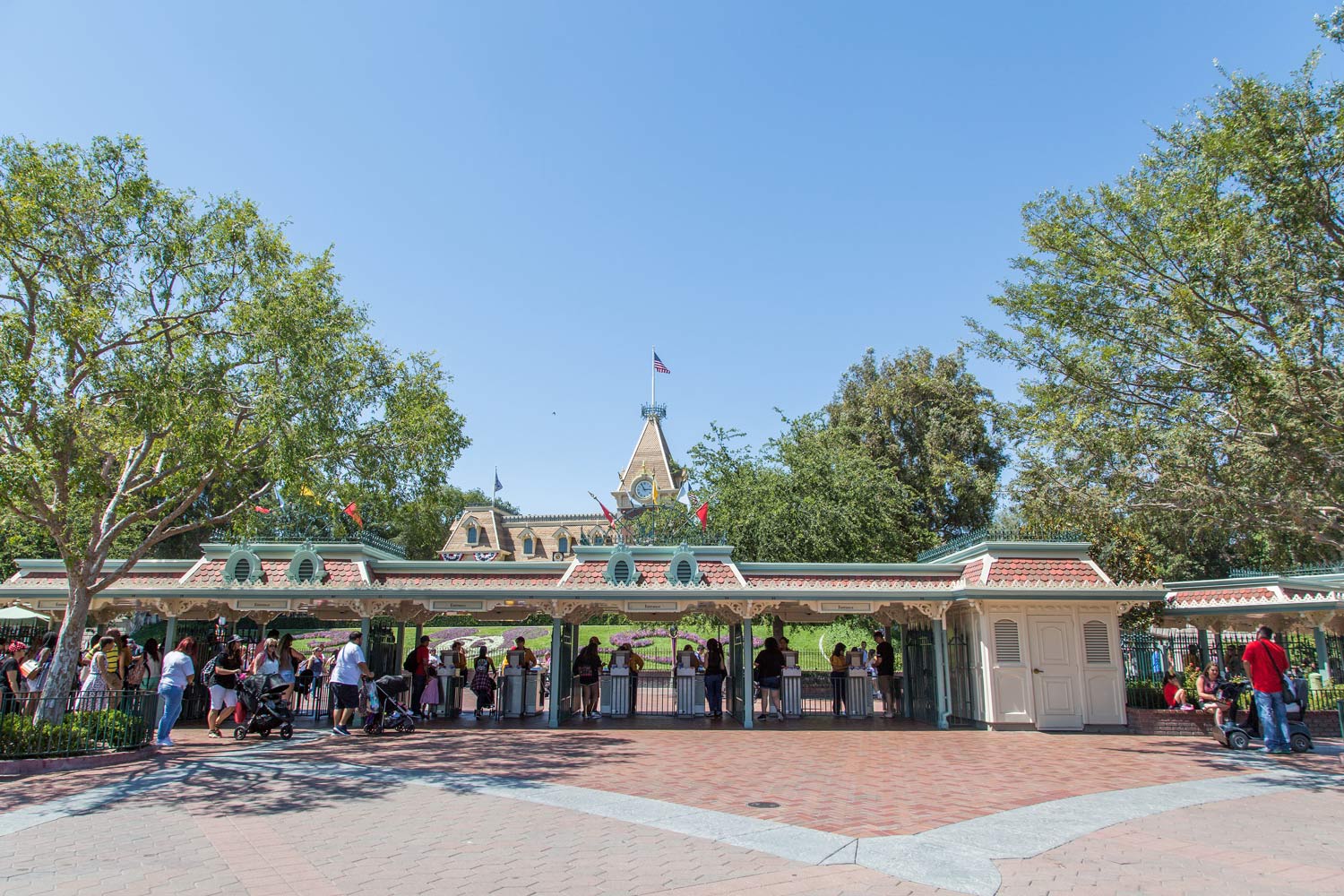 Crowd entering Disneyland gate under blue sky, with castle and green-trimmed archway in view