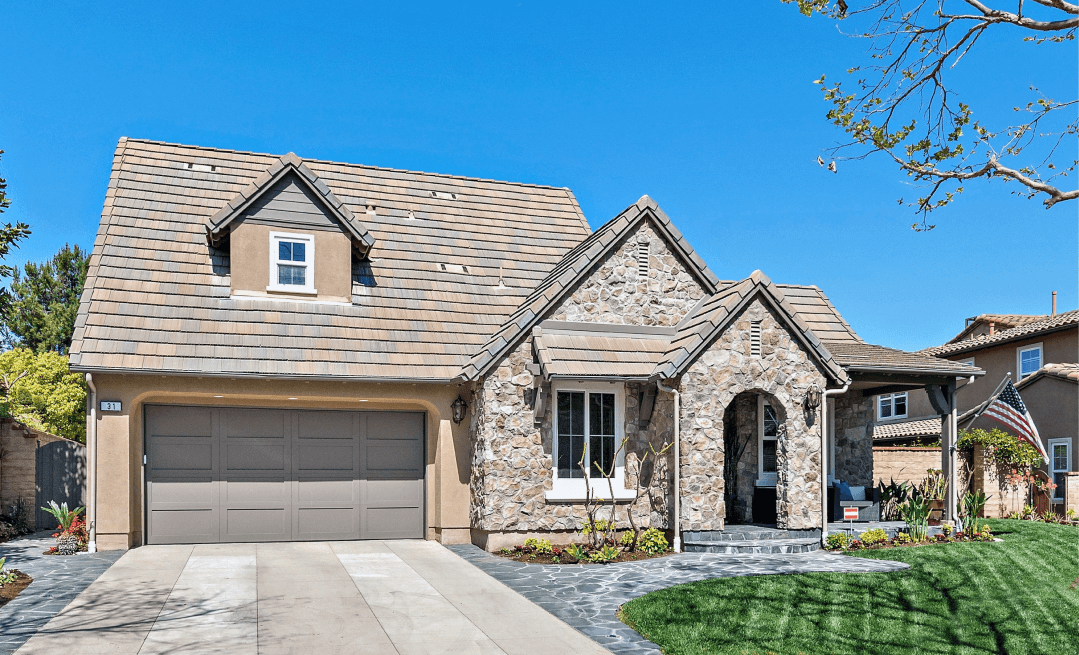 Stone-front suburban house with gray roof, two-car garage, and front lawn under a clear blue sky