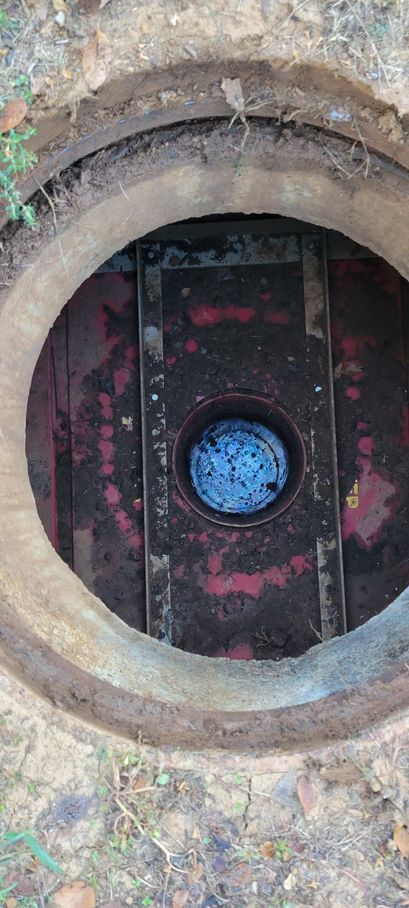 Open manhole with a blue circular valve visible inside, set in a rough concrete surface.