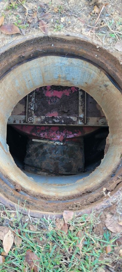 Open circular manhole with rusted rim revealing a dark utility chamber and pink markings inside