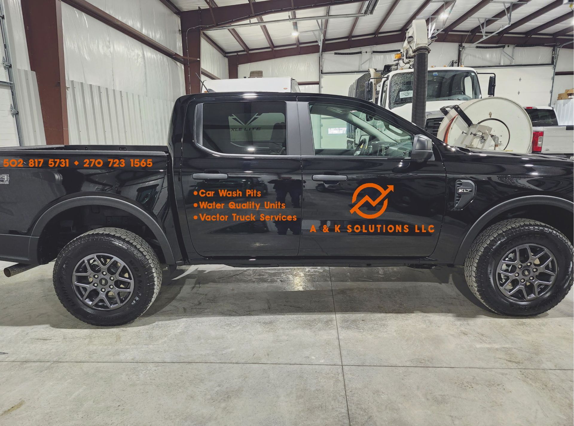 Black pickup truck with orange company lettering parked inside a workshop garage.