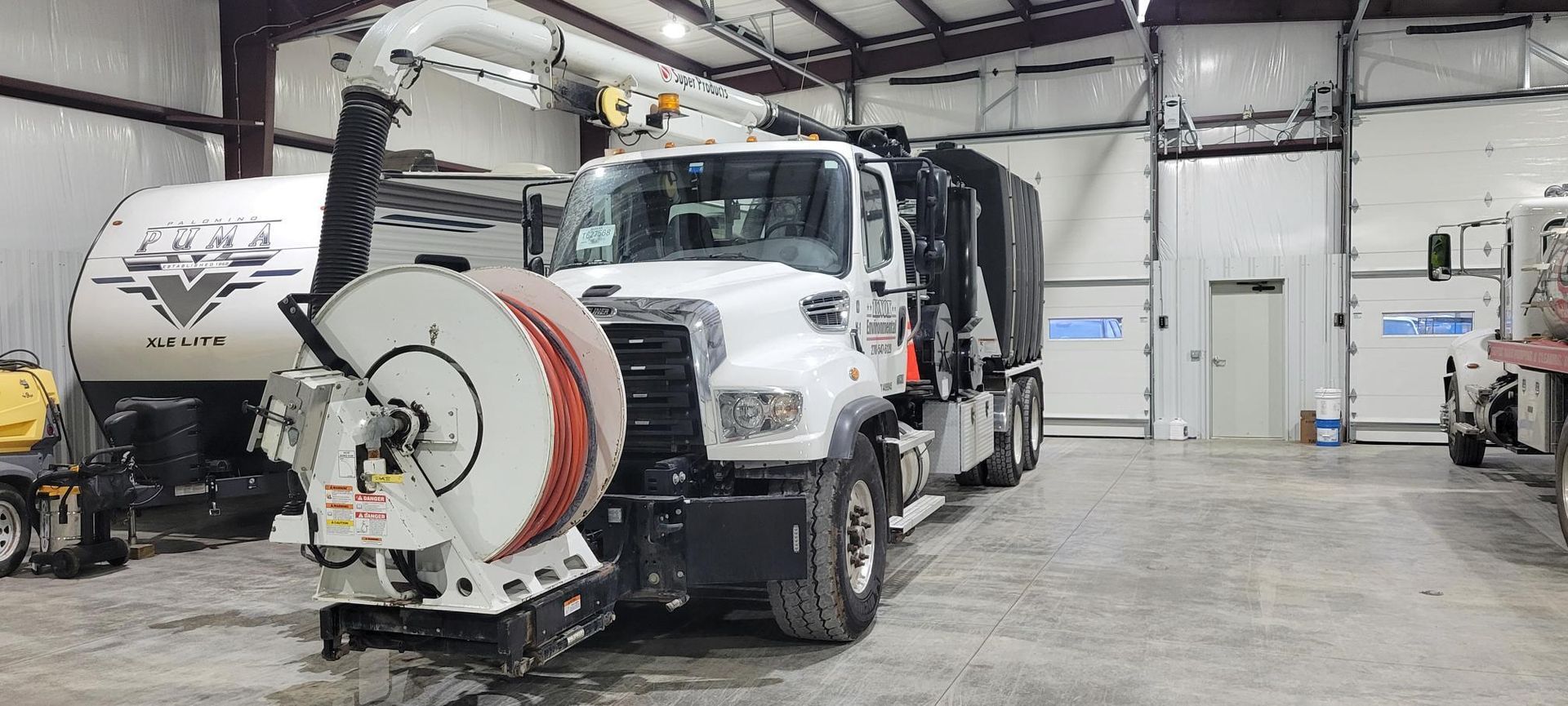 White utility truck with a large street sweeper attachment parked inside a maintenance garage