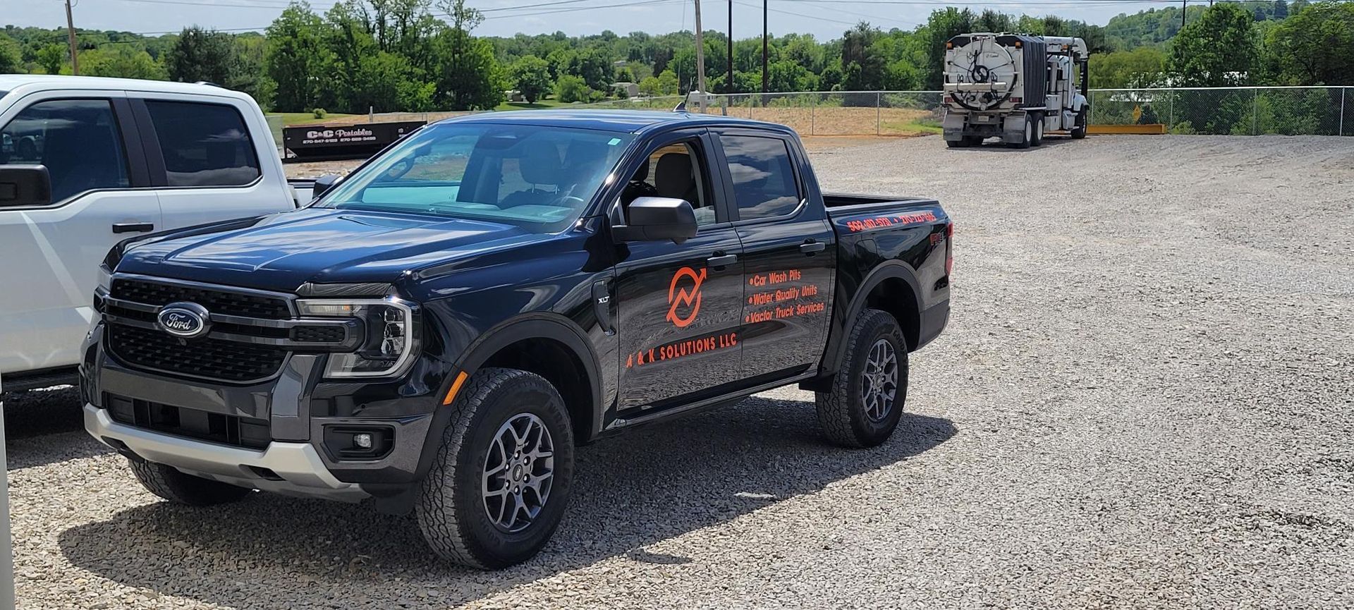 Black GMC pickup truck with orange decals parked on a gravel lot under a clear sky