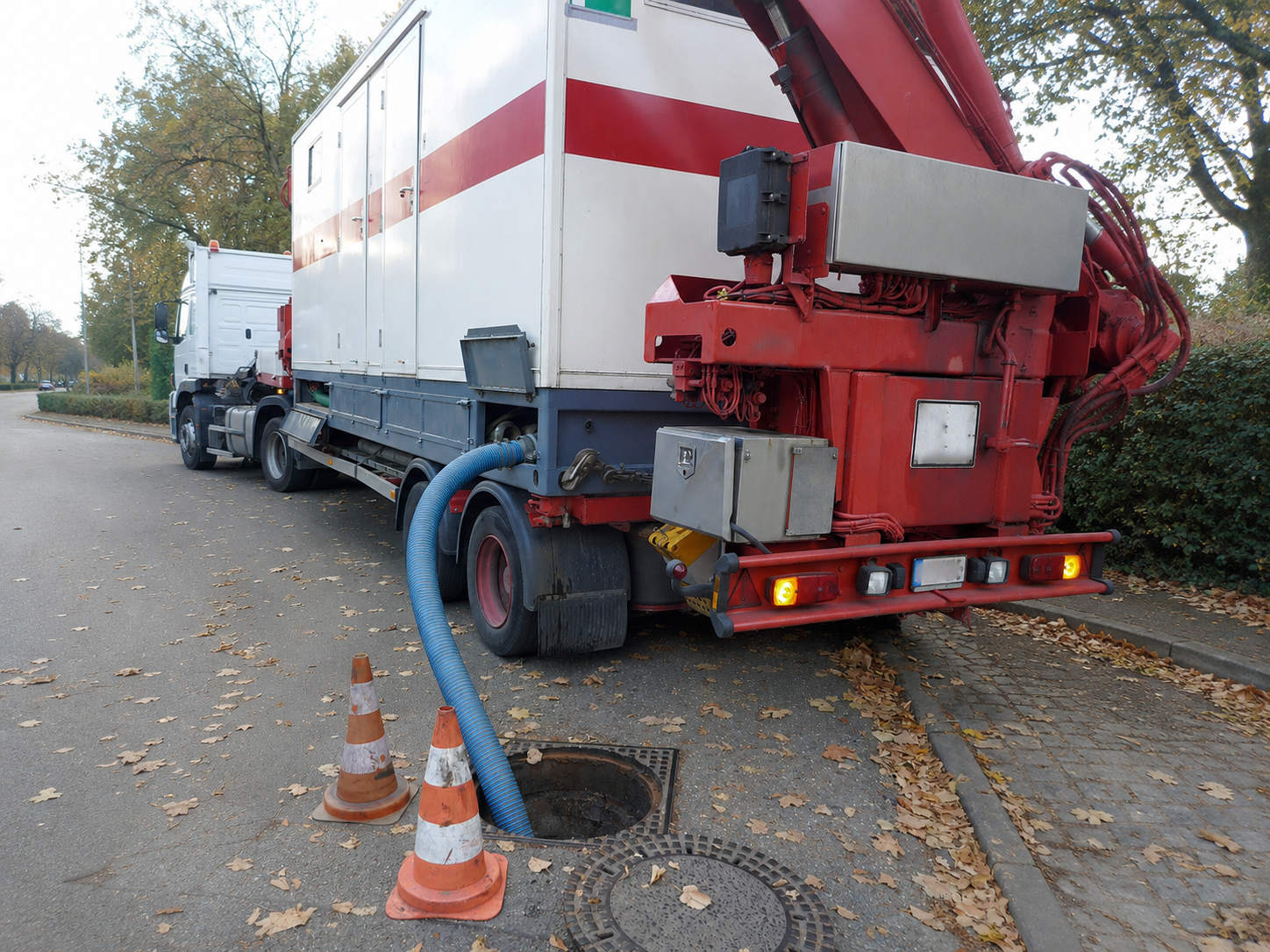 Large red-and-white utility truck beside train tracks, with hoses and traffic cones on an autumn street.