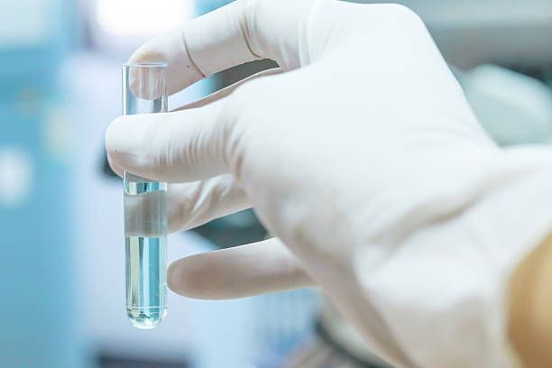 Gloved hand holding a small vial of blue liquid in a lab setting