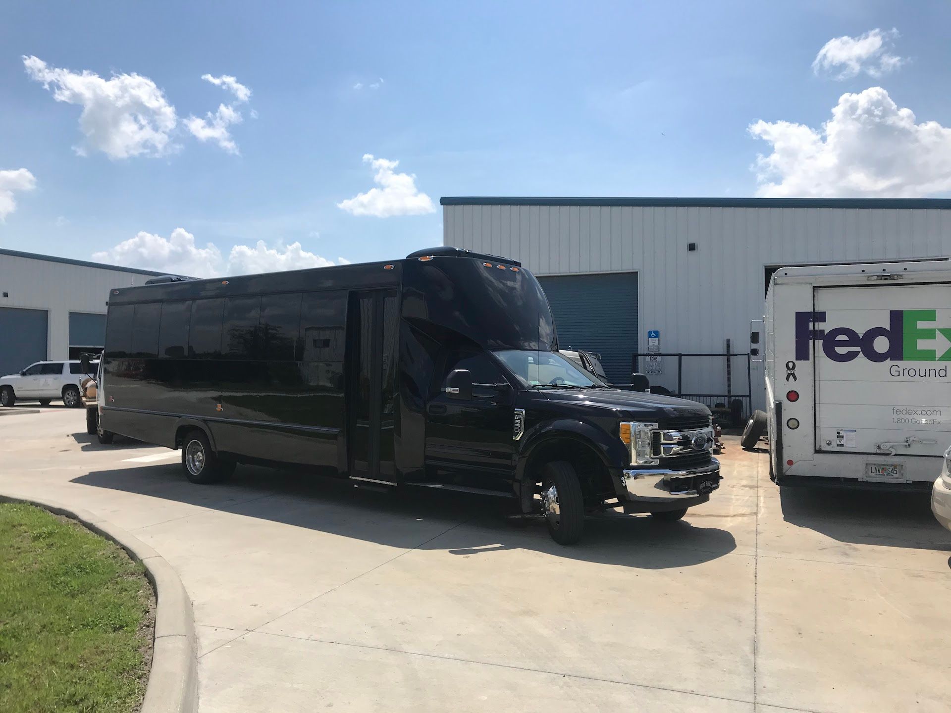 Black party bus parked outside of a building, next to a FedEx truck, on a sunny day. | East Coast Motorworks