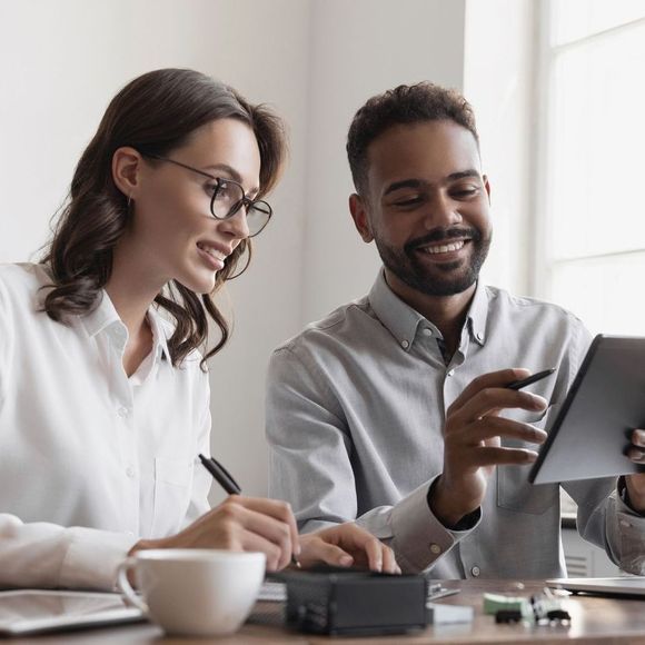 A man and a woman are sitting at a table looking at a tablet.
