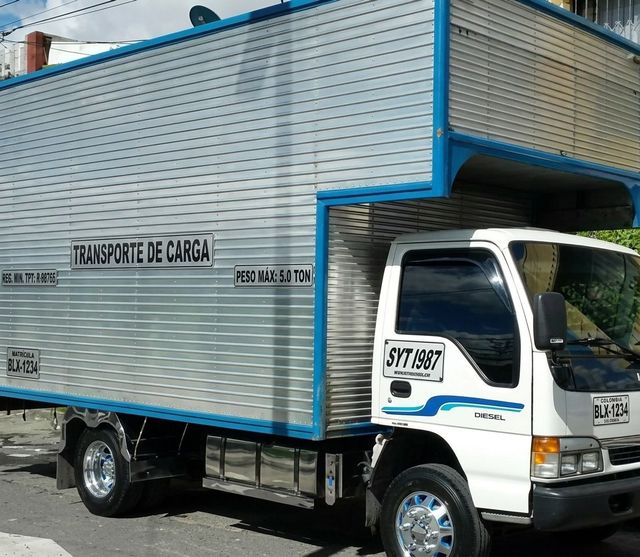 Camión de carga blanco con detalles azules estacionado en una calle, vista lateral de la caja con texto en el panel.