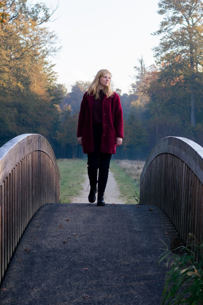 Een vrouw in een rode jas loopt over een houten brug.