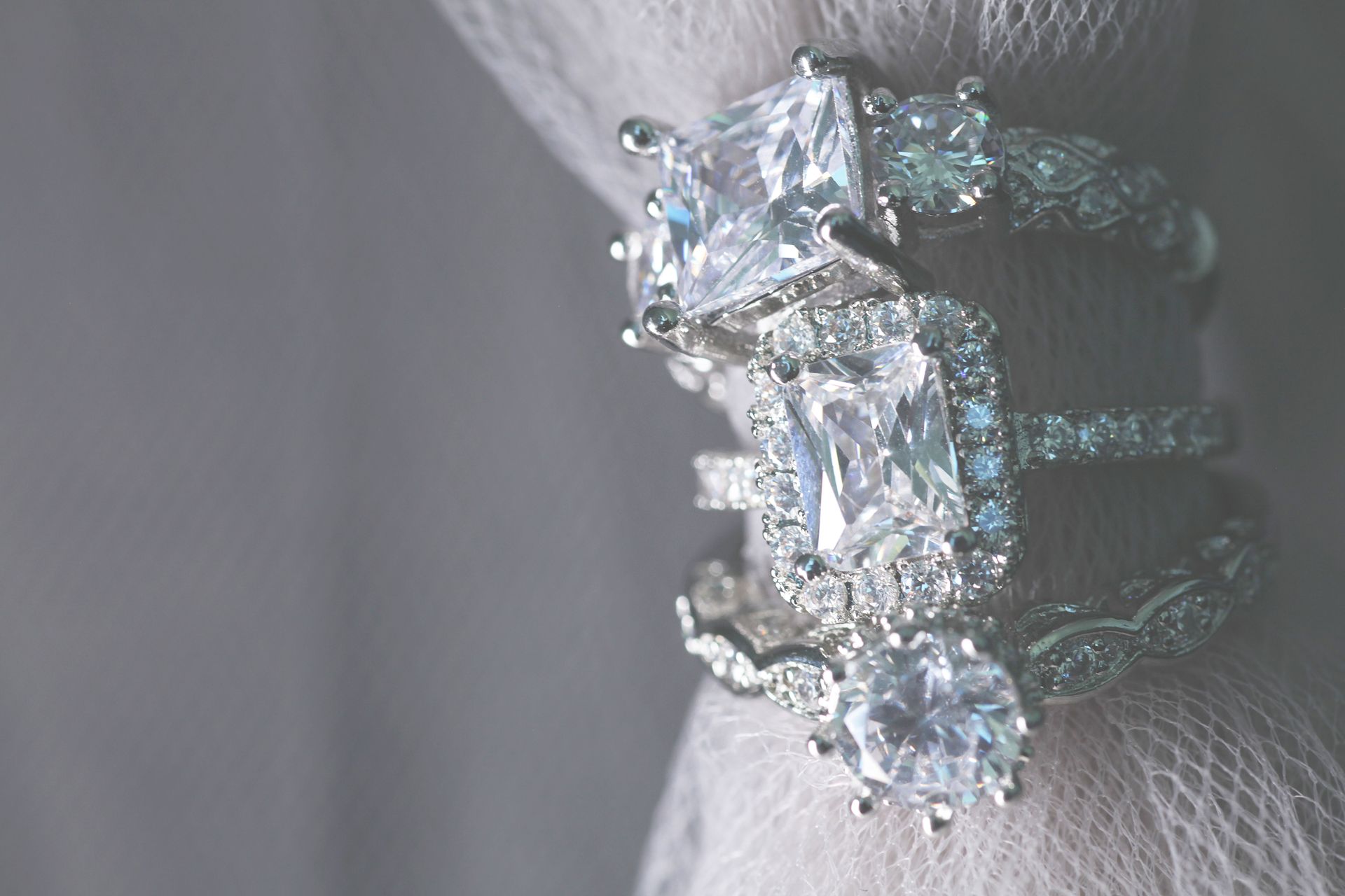 Several diamond wedding engagement rings wrapped around a grey cloth.