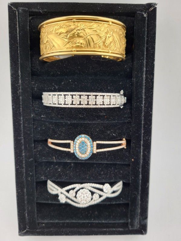 Jewelry display: gold cuff, diamond tennis bracelet, rose gold and blue gem bracelet, silver floral bracelet.