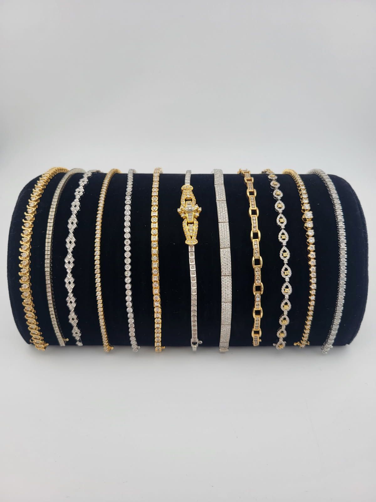 Collection of diamond and gold bracelets displayed on a black velvet cylindrical stand.