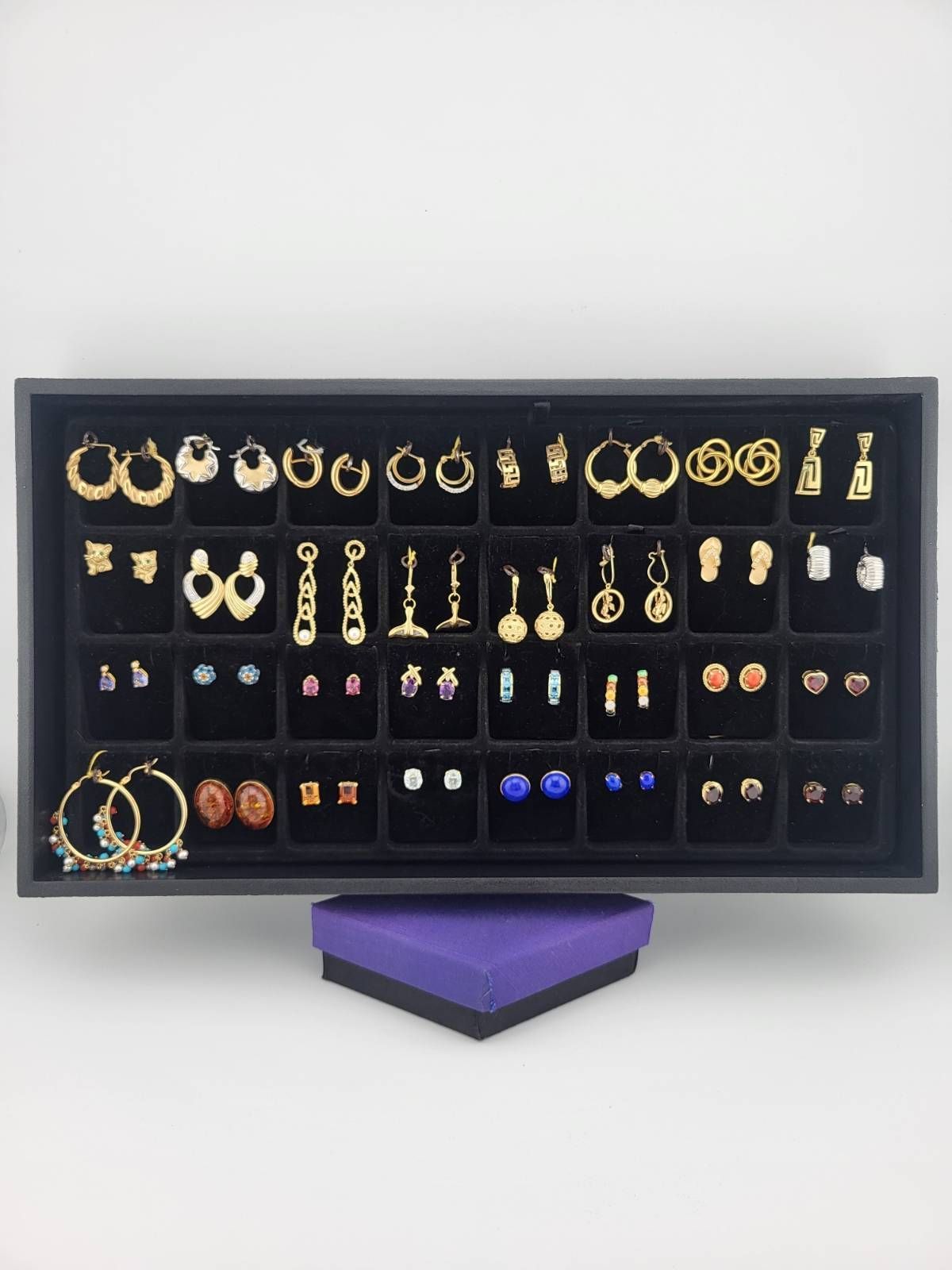 A display tray of various gold earrings in a black tray, with a purple box underneath.