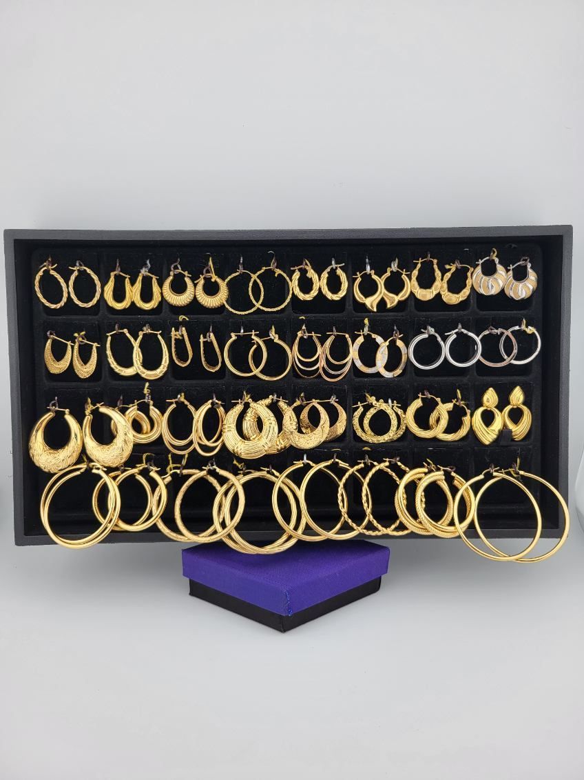 Black display case filled with rows of gold hoop earrings and a few silver ones on a purple stand