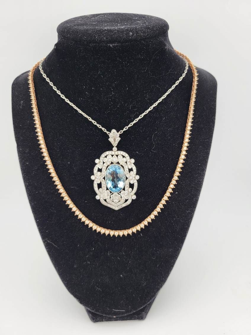 Two layered necklaces on a black velvet display bust, one with a blue gemstone pendant.