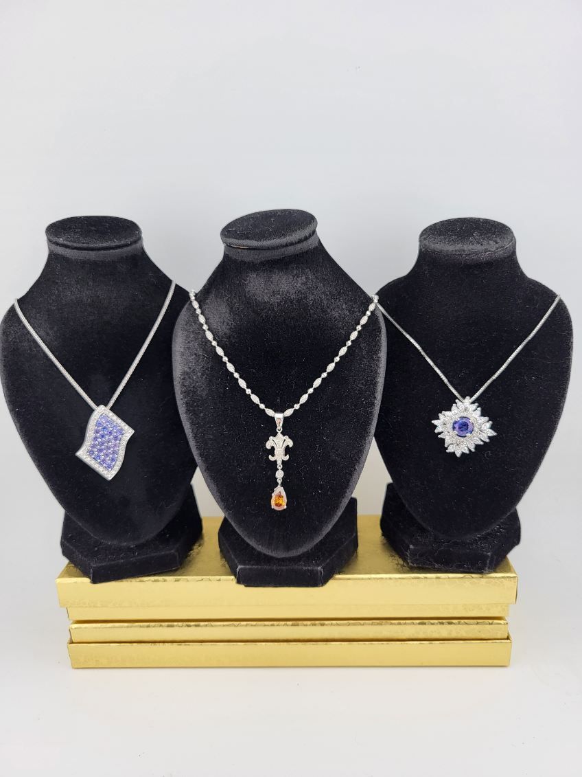 Three black necklace stands displaying silver pendant necklaces on a wooden base.