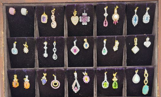 Tray of assorted colorful dangling earrings arranged in compartments on a dark background