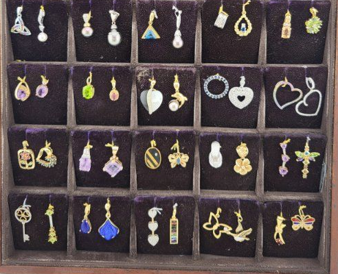 Display of assorted dangling earrings in black velvet compartments, featuring hearts, stars, flowers, and gemstones.
