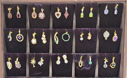 Tray of assorted dangling earrings in gold, green, purple, and white, arranged in compartments.
