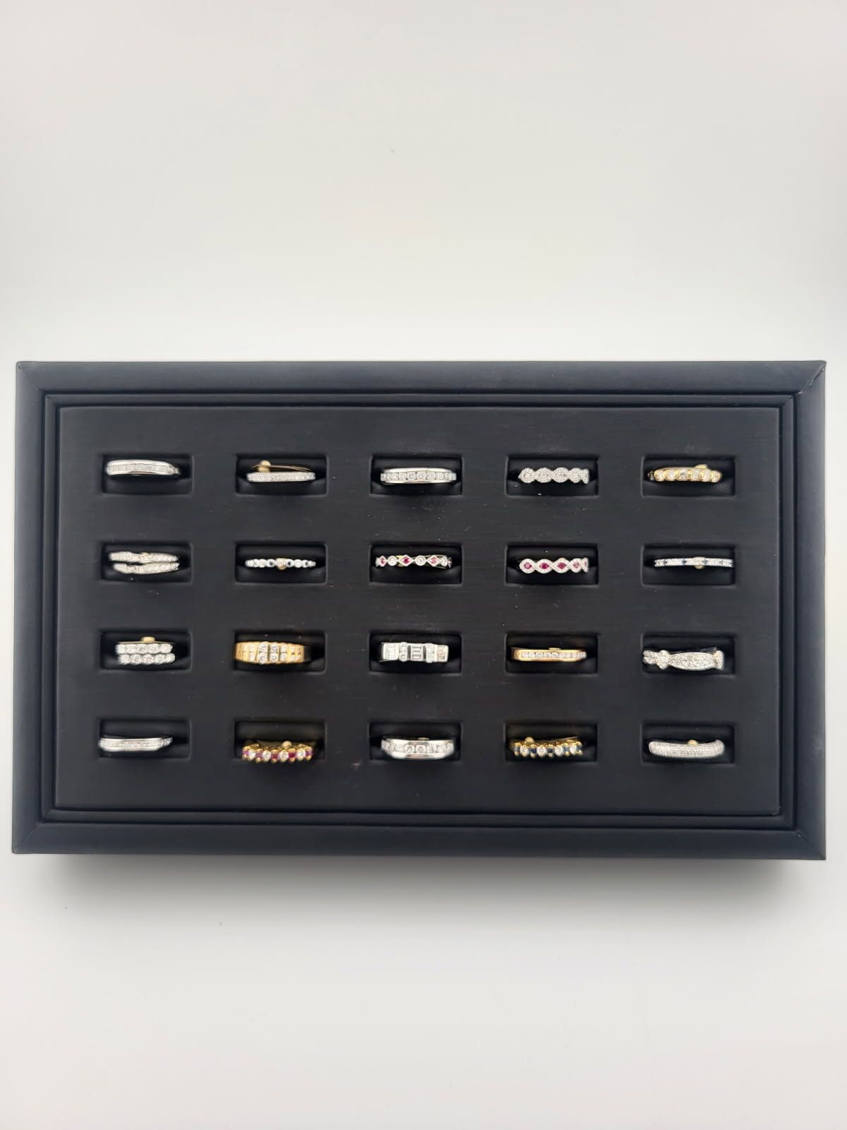 Black-framed display case with multiple small rings arranged in a grid on a light wall.