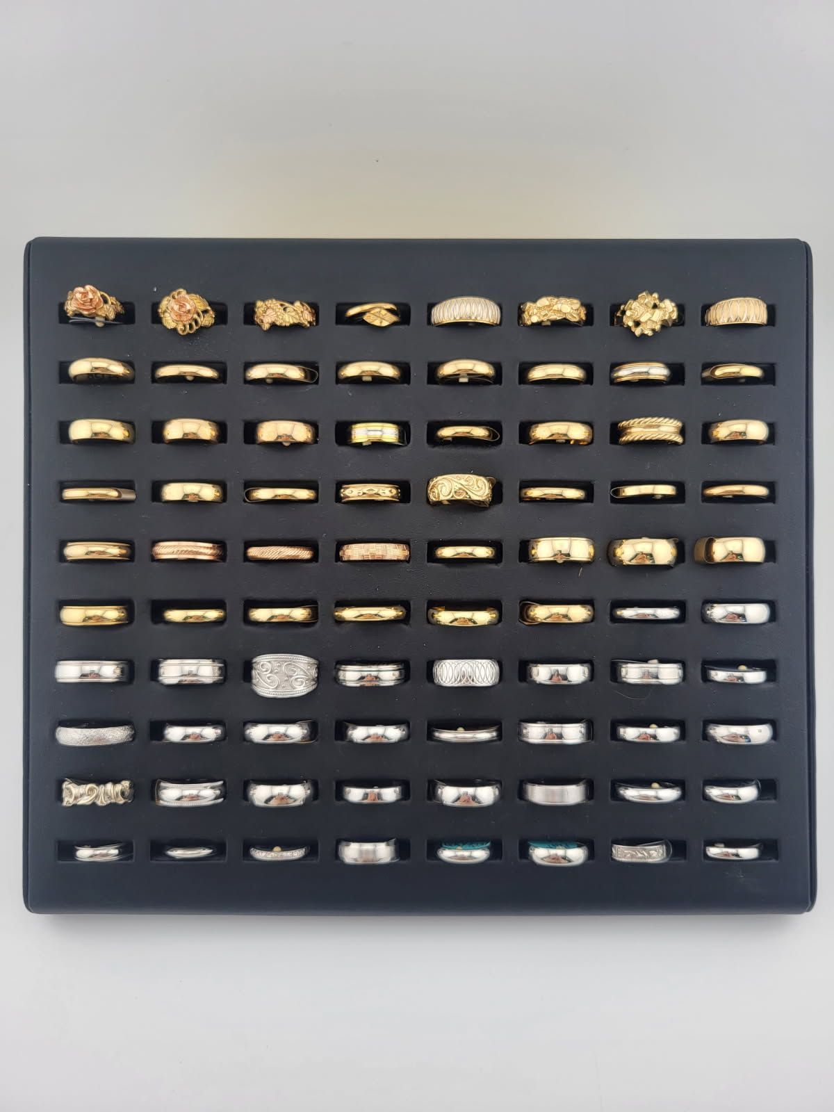 Dark display board with rows of small gold and silver objects, likely pins or charms, on a light wall