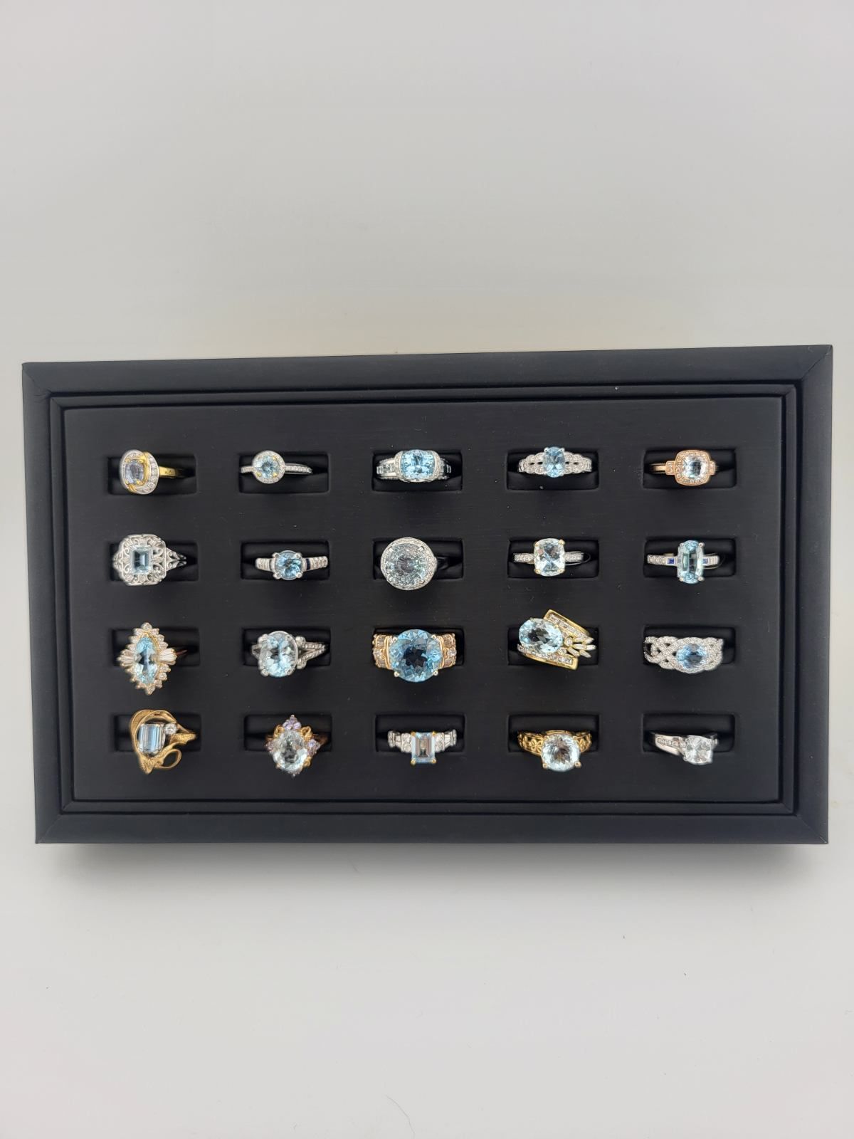 Black tray displays twenty-four aquamarine gemstone rings.