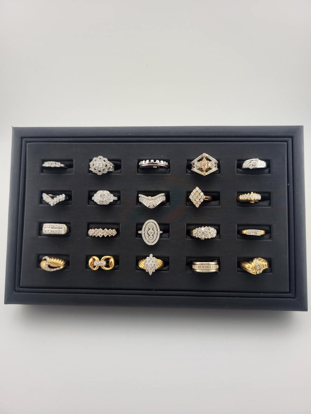 Black framed display of assorted gold and silver rings arranged in rows on a white background